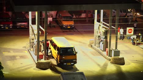 Vista-Real-De-Una-Gasolinera-Por-La-Noche-Con-Asistentes-Alimentando-Un-Autobús-Comercial-En-África,-Ghana