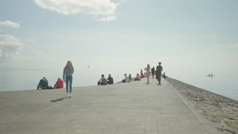 People-enjoying-a-day-at-the-seaside-as-two-canoes-row-past,-wide-shot