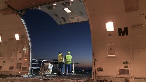 Two-workers-waiting-on-open-ramp-of-a-cargo-airplane,-concept-night-delivery