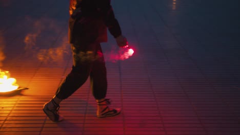 Un-Hombre-Vestido-De-Negro-Prende-Varios-Fuegos-En-El-Suelo,-Preparando-Un-Espectáculo-De-Fuego-En-Una-Plaza