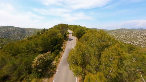 Filmische-FPV-Luftaufnahme-Eines-Autos,-Das-Eine-Malerische-Bergstraße-Entlangfährt