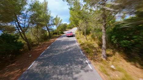 Vista-Aérea-Cinematográfica-Siguiendo-Un-Clásico-Mustang-Rojo-A-Través-Del-Pintoresco-Paisaje-Montañoso-En-España