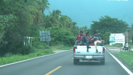 Tres-Hombres-Viajando-En-La-Parte-Trasera-De-Una-Camioneta-Llena-De-Carga-En-Una-Carretera-De-Dos-Carriles-Cerca-De-La-Costa,-Vista-Del-Tablero