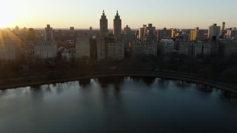 Aerial-view-tilting-over-the-Central-park-Reservoir,-toward-the-El-Dorado-building,-sunset-in-New-York,-USA