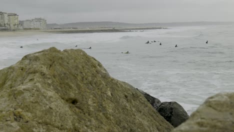 Grupo-De-Surfistas-Esperando-La-Mejor-Ola-Pov-Detrás-De-Las-Rocas