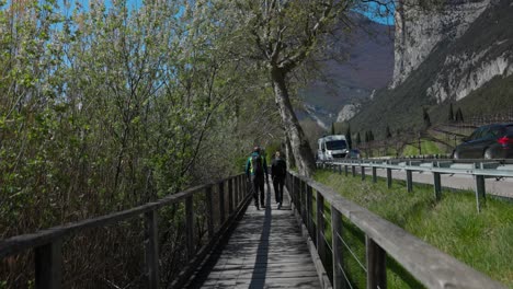 Rückansicht-Eines-Wanderpaares,-Das-über-Einen-Hölzernen-Laufsteg-In-Der-Nähe-Einer-Stark-Befahrenen-Straße-Am-Tobliner-See-Im-Trentino,-Italien,-Läuft