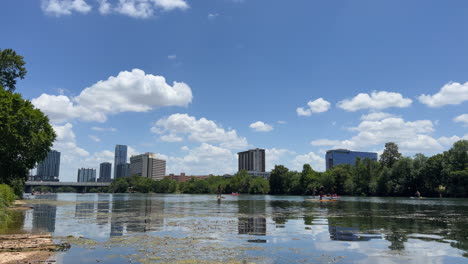 Los-Practicantes-De-Remo-Flotan-Hacia-Abajo-En-El-Lago-Lady-Bird-Con-El-Horizonte-Del-Centro-De-Austin,-Texas,-Detrás-De-Ellos