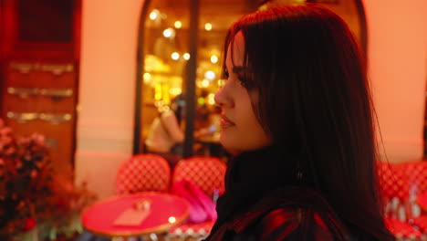 Portrait-of-a-beautiful-young-woman-looking-at-the-camera-in-front-of-a-restaurant,-in-Paris-near-Montmartre,-at-night