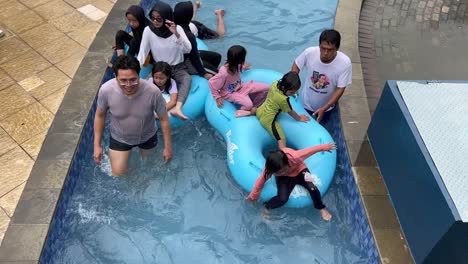 Tourist-enjoying-wavy-pool-using-inflatables-in-swimming-pool,-family-having-fun-during-summer-holiday-at-waterpark