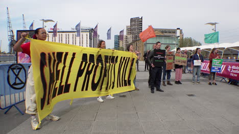 Aktivisten-Des-Klimawandels-Halten-Ein-Gelbes-Banner-Mit-Der-Aufschrift-„Shell-Profite-Töten“-Neben-Anderen-Demonstranten,-Die-Plakate-Vor-Der-Jahreshauptversammlung-Von-Shell-Im-Excel-Ausstellungszentrum-Halten