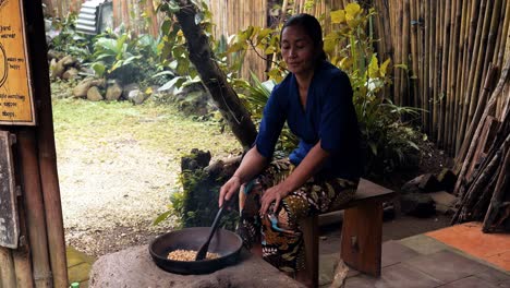 Slow-motion-handheld-shot-of-an-indonesian-employee-of-a-coffee-plantation-roasting-and-preparing-coffee-beans-of-the-expensive-kopi-luwak-coffee-in-a-wok-with-a-wooden-spoon