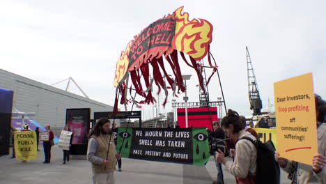 Aktivisten-Des-Klimawandels-Halten-Ein-Farbenfrohes-Banner-Mit-Der-Aufschrift-„Willkommen-In-Der-Hölle“-Neben-Demonstranten,-Die-Banner-Und-Plakate-Vor-Der-Shell-Jahreshauptversammlung-Im-Excel-Ausstellungszentrum-Hochhalten