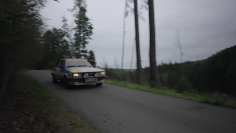 Camera-follows-vintage-car-speeding-through-narrow-forest-asphalt-road-at-rally