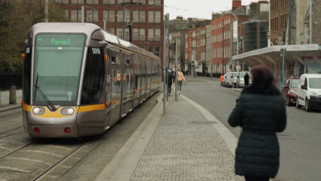 Frau-Geht-Von-Der-Kamera-Weg,-Als-Sich-Ein-öffentlicher-Zug-In-Dublin,-Irland,-Nähert