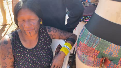 An-Amazonian-indigenous-woman-sits-in-the-marketplace-with-her-face-and-arms-completely-painted-with-ritual-paintings