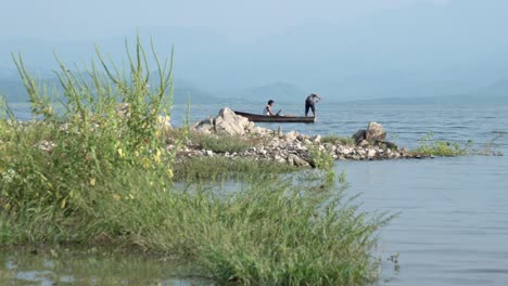 Zwei-Fischer-Ziehen-Auf-Einem-Kleinen-Boot-Nach-Links-Rudernd-Netze-Aus-Dem-Meer,-Schwenk-Nach-Links