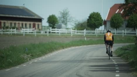 Cyclist-in-yellow-jersey-on-road-bike-pedals-down-calm-country-road