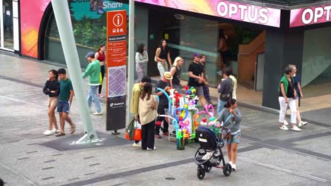 Busker-selling-artistic-balloon-twisters-with-special-model-shape-on-the-street-at-Queens-street-mall,-busy-weekend-crowds-at-downtown-Brisbane-city,-Queensland,-Australia