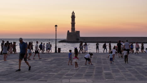 Menschen-Auf-Der-Promenade-Bei-Sonnenuntergang,-Leuchtturm-Im-Hintergrund,-Chania