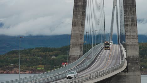 Los-Coches,-Un-Camión-Pesado-Que-Transporta-Una-Topadora-Y-Una-Casa-Rodante-Pasan-Por-Las-Curvas-Del-Puente-Halogaand-Sobre-El-Fiordo.