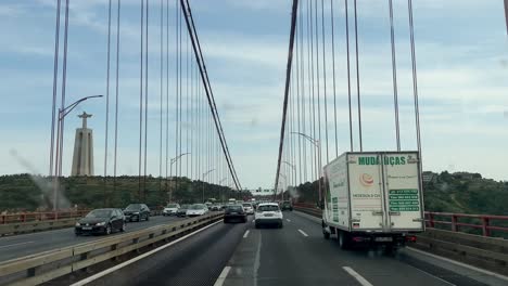 POV-Fahrt-Auf-Der-Berühmten-Brücke-Ponte-25-De-April-In-Lissabon-Und-Die-Christus-König-Statue-Im-Hintergrund