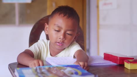 Niño-Leyendo-Y-Escribiendo-Solo-En-La-Mesa