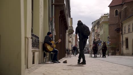 Músico-Callejero-Interpretando-Una-Canción-De-Guitarra-En-El-Casco-Antiguo,-Mientras-Un-Joven-Le-Da-Dinero