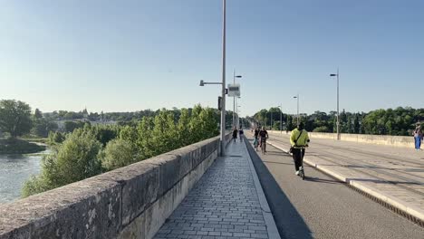 Scooter-Eléctrico-En-Cámara-Lenta-Y-Ciclistas-En-El-Puente-Wilson-En-La-Ciudad-De-Tours,-Francia