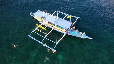 Aerial,-young-Tourists-Group-having-fun-on-island-hopping-tour-in-El-Nido-jumping-off-Boat-and-swimming-in-Crystal-Clear-tropical-water