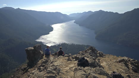 Dos-Jóvenes-Sentados-En-Una-Pintoresca-Cresta-Con-Vistas-Al-Hermoso-Lago-De-Montaña