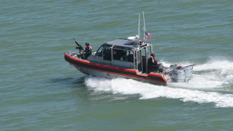 Primer-Plano-De-Un-Barco-De-Alta-Velocidad-De-La-Guardia-Costera-Estadounidense-Que-Atraviesa-Las-Olas-Del-Océano,-Con-Un-Valiente-Soldado-De-Pie-Fuerte,-Armado-Con-Una-Ametralladora.-Fuerza-Armada-De-La-Guardia-Costera-Estadounidense-De-Servicio