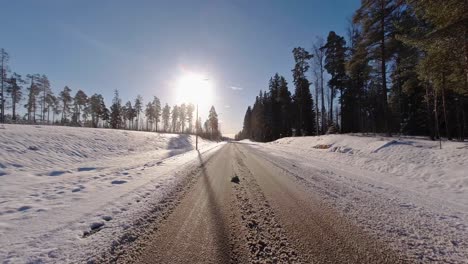 El-Coche-Circula-Por-La-Carretera-En-Invierno,-Flanqueado-Por-árboles-A-Ambos-Lados,-Mientras-El-Sol-Proyecta-Su-Resplandor-Radiante