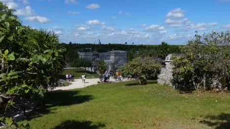 Tourists-around-Temple-of-the-Frescoes-at-Tulum-archeological-site,-Quintana-Roo,-Mexico