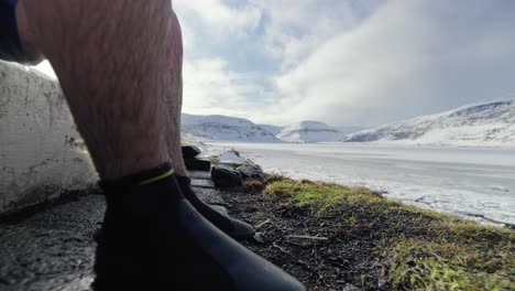 Man-putting-on-neoprene-shoes,-near-a-hot-pot-with-mountains-in-a-distance