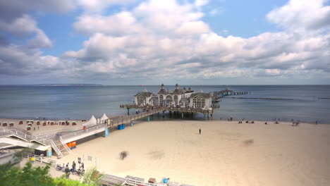 Touristen-Besuchen-Die-Seebrücke-Sellin-Und-Spazieren-Am-Weichen,-Weißen-Sandstrand-Der-Insel-Rügen-An-Der-Ostseeküste,-Deutschland---Zeitraffer-Weitwinkel-Erhöhungsansicht