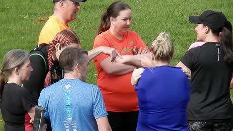 Group-of-runners-gathered-speaking-and-supporting-each-other-in-local-park-field-at-start-of-their-fitness-run