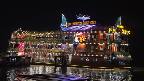 A-colorful-floating-restaurant-ship,-illuminated-by-colorful-LED-lights-on-the-river-at-night