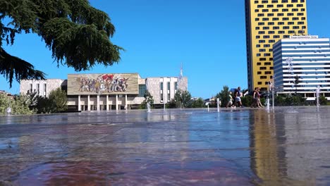 La-Gente-Se-Refresca-Frente-A-Las-Fuentes-En-El-Centro-De-La-Capital-Tirana-En-Los-Calurosos-Días-De-Verano,-El-Museo-Nacional-Y-Los-Altos-Edificios-De-La-Ciudad