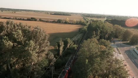 Cautivadoras-Imágenes-Aéreas-De-Drones-Siguen-A-Un-Tren-Cisterna-De-Carga-Cargado-Que-Pasa-A-Través-De-Vastos-Campos-De-Maíz-Iluminados-Con-Luz-Dorada,-Mientras-El-Dron-Se-Eleva,-Revelando-El-Impresionante-Paisaje-Rural.