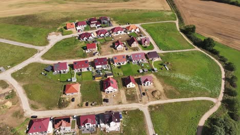 Kleine-Neue-Wohnsiedlung-Am-Rande-Der-Stadt,-Sonniger-Tag,-Grüne-Felder,-Neue-Straßen,-Drohne,-Neigung-Nach-Unten