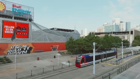 Vista-Aérea-De-Un-Tren-Del-Metro-De-Houston-Que-Pasa-Frente-Al-Estadio-Shell-Energy-En-El-Centro-De-Houston,-Texas