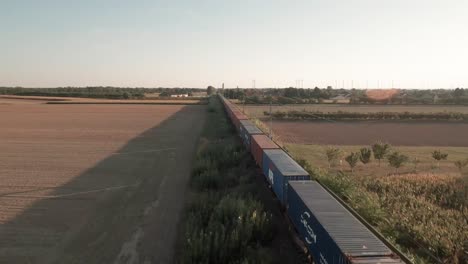 Viaje-Cargado:-Imágenes-Aéreas-Siguen-Un-Tren-De-Carga-Cargado-De-Contenedores-A-Través-De-Vastos-Campos-De-Maíz-Iluminados-Con-Luz-Dorada.