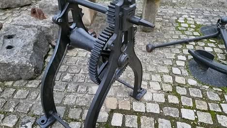 Vintage-black-iron-laundry-mangle-machinery-displayed-on-cobblestone-path-outside-museum