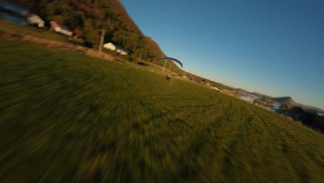 Toma-De-Seguimiento-Aéreo-Que-Muestra-El-Aterrizaje-De-Parapente-En-El-Valle-Del-Fiordo-De-Noruega-Durante-La-Puesta-De-Sol.