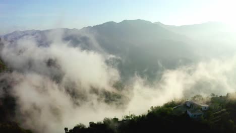 Luftaufnahme-Einer-Drohnenkamera,-Viel-Nebel-Und-Berge-Sind-Zu-Sehen,-Und-In-Den-Hügeln-Sind-Auch-Häuser-Zu-Sehen