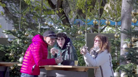 A-family-of-three-enjoying-some-food-at-the-Christmas-market-in-Meran---Merano,-South-Tyrol,-Italy