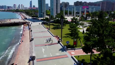 Aerial-tour-over-Xingfu-seaside-park-with-skyrise-cityscape-background-in-Weihai,-China