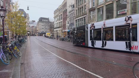 Tranvía-O-Tren-Circulando-Por-Una-Calle-Central-De-Amsterdam-Y-Un-Ciclista-Caminando