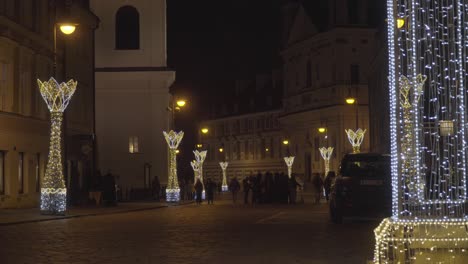 Christmas-Lighting-Decoration,-Old-Cobblestone-Streets-of-Old-Town-Warsaw-Poland-with-People-Walking-by