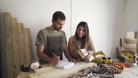 Two-people-at-a-carpenter's-desk-workbench-draw-up-plan-for-a-renovation-project